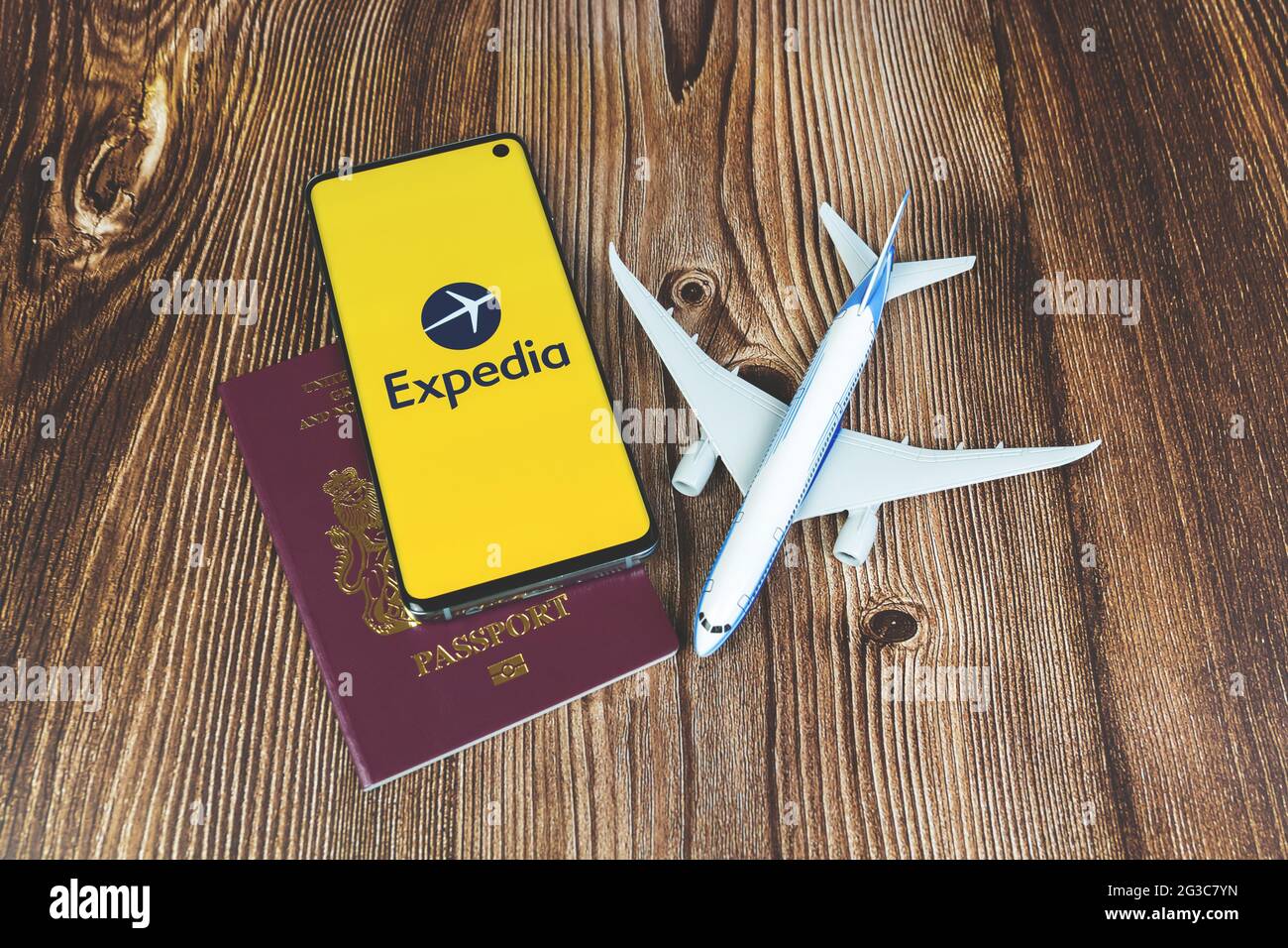 Smartphone mit Expedia App-Logo mit Flugzeugspielzeug und rotem Reisepass auf Holzhintergrund. Reise-Anwendung, Urlaubsplanung Stockfoto