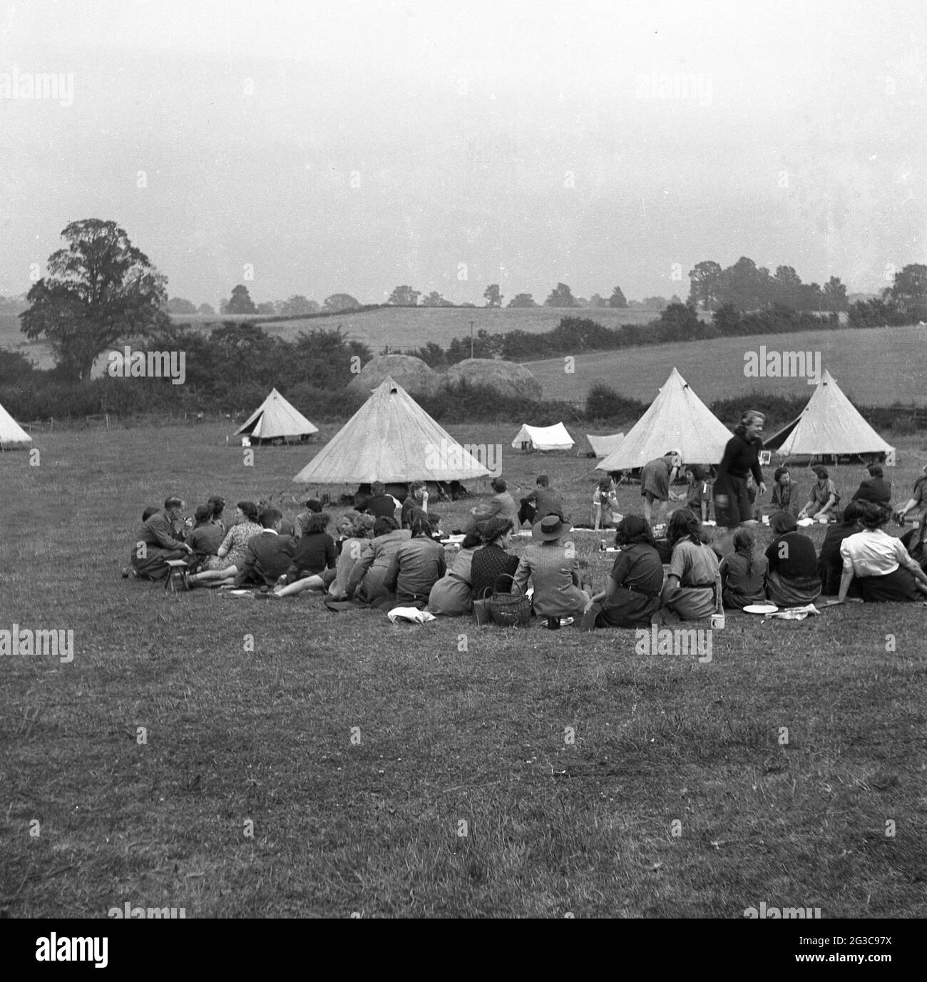 In den 1950er Jahren, in England, Großbritannien, lagern die Mädchen, Eltern und Familie zusammen mit den Mädchen, die draußen auf einem Feld bei einer Reihe von Wigwam-förmigen Zelten sitzen. Stockfoto