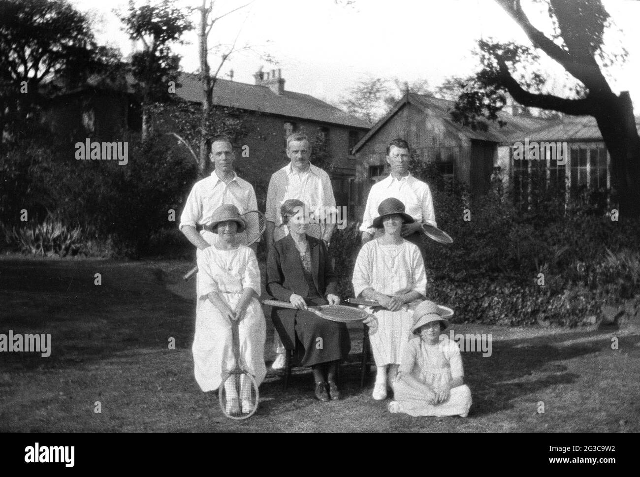 1930s, historisch, Männer und Frauen Tennisspieler, Sozialspieler, in den Tennis-Outfits der Zeit, lange Röcke, mit ihren Holzschlägern, sitzen zusammen in einem Garten für ein Foto, in der Regel formell, wie es die Norm in dieser Zeit war, England, Großbritannien. Stockfoto