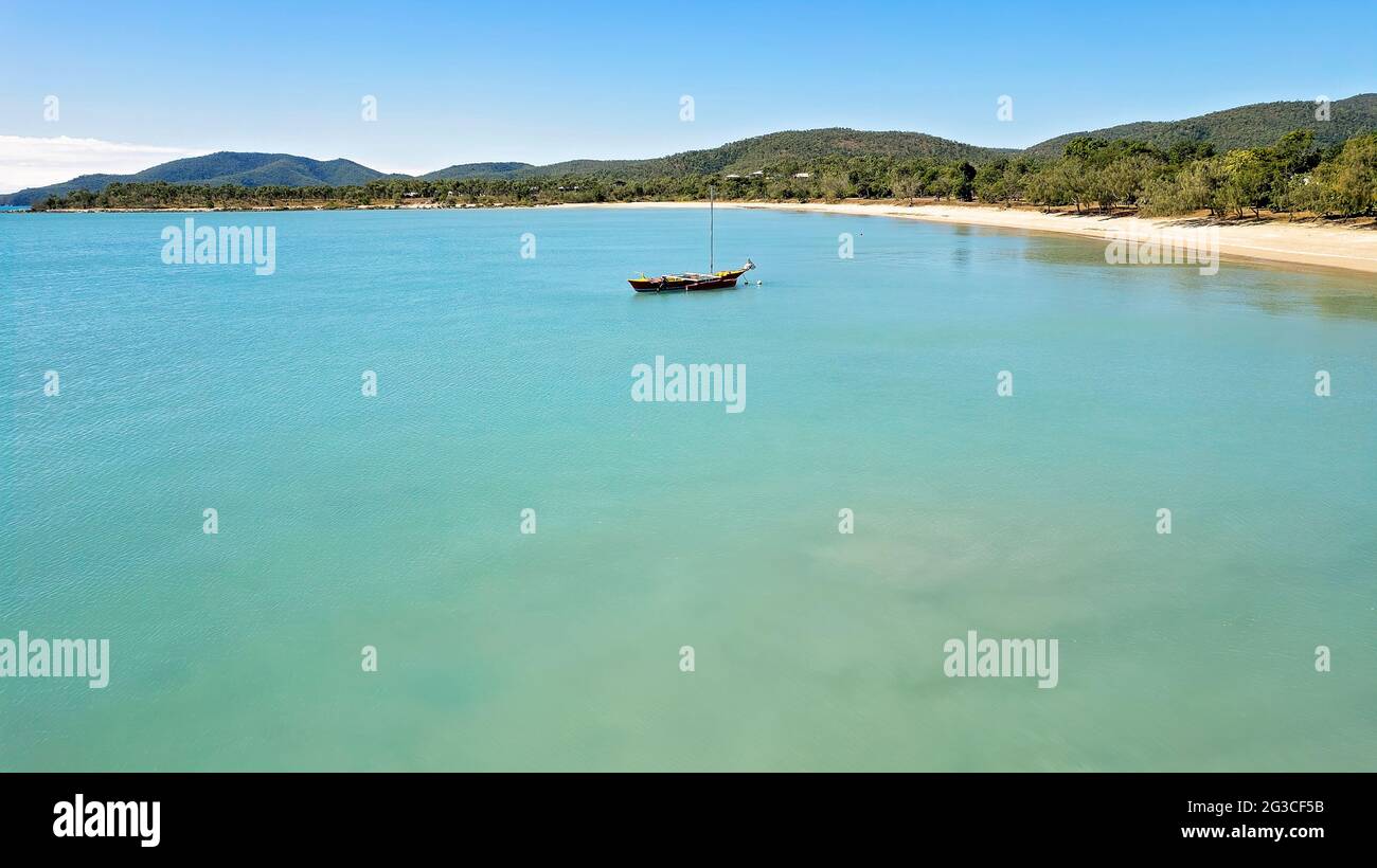 Ein farbenfrohes Boot vor der Küste vor einem ruhigen, blauen Meer vor einer sandigen Strandküste vor Anker Stockfoto