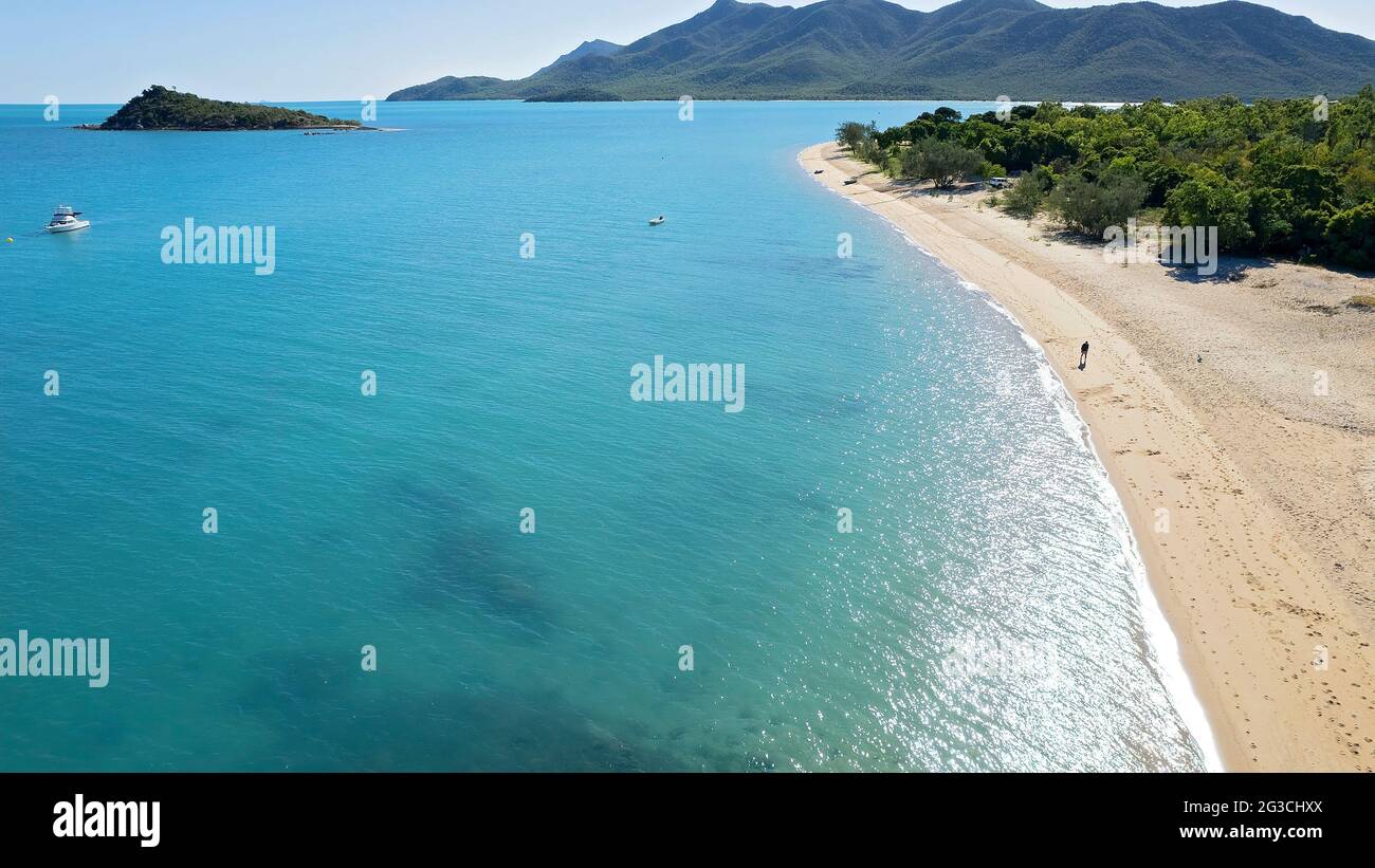 Ein Mann, der auf einem Sandstrand neben dem klaren blauen Meer mit Licht am frühen Morgen Licht glitzert auf dem Wasser und Boote vor Anker vor der Küste von BU Stockfoto