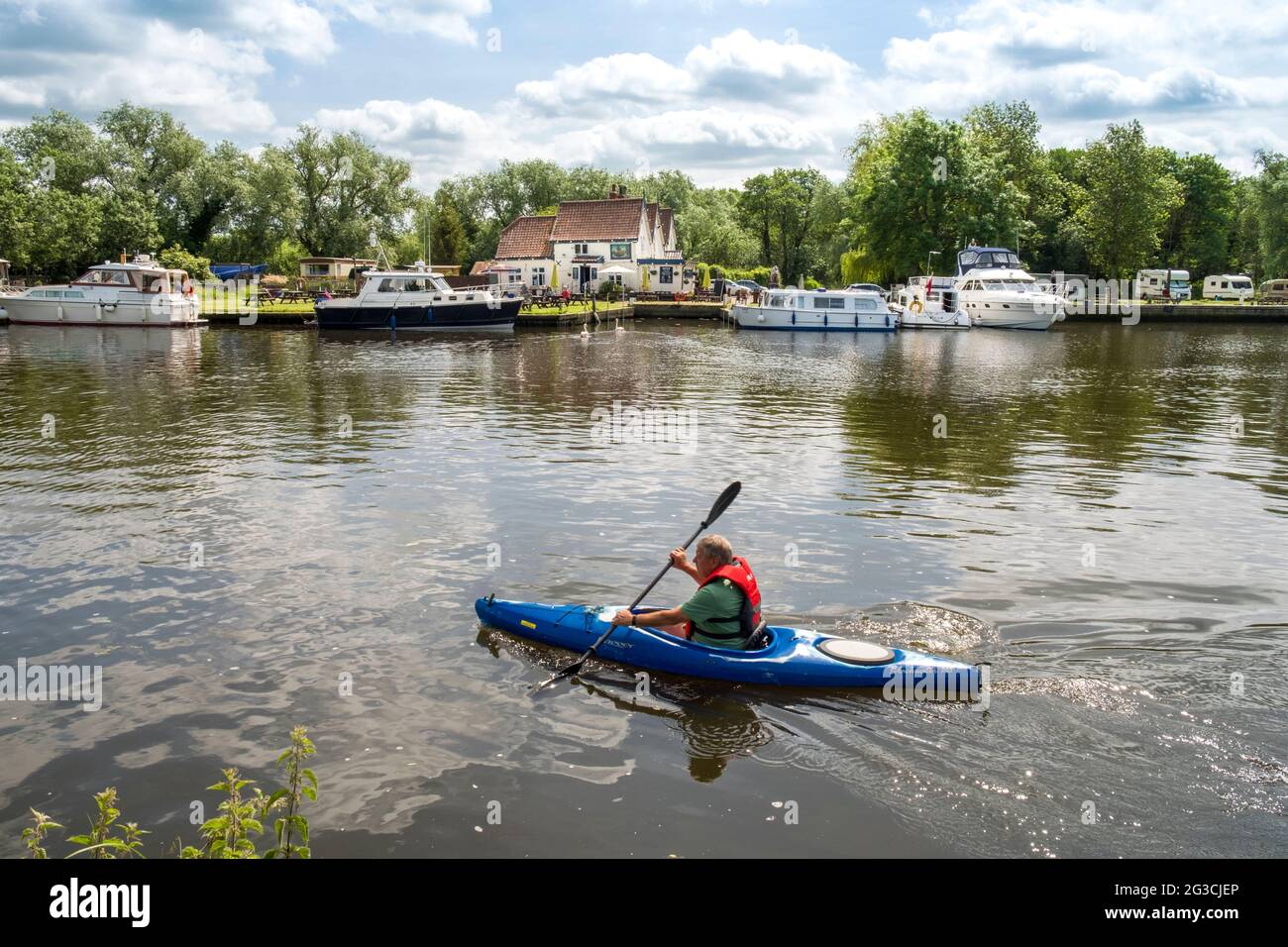 Kanufahren auf dem Fluss Yare, Norfolk. Auf der anderen Seite befindet sich das Ferry House, Surlingham, Norfolk, Großbritannien. Ein Pub am Fluss Yare an den Norfolk Broads. Stockfoto