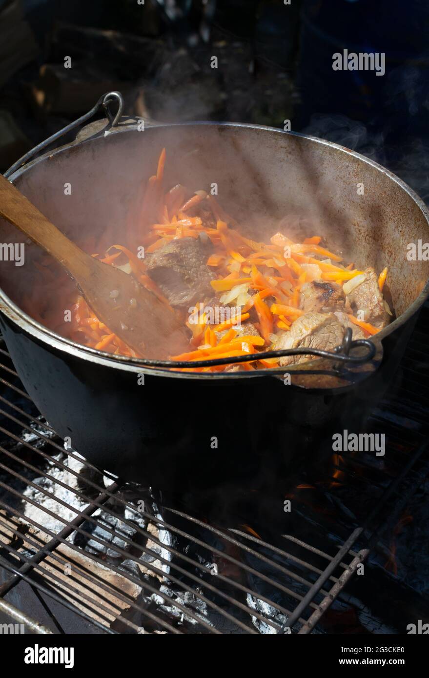 Kochen traditioneller orientalischer Pilaf in einem Kessel über einem Feuer. Große Fleischstücke und fein gehackte Zwiebeln und Karotten werden über Holzkohle geschmort. Zer Stockfoto