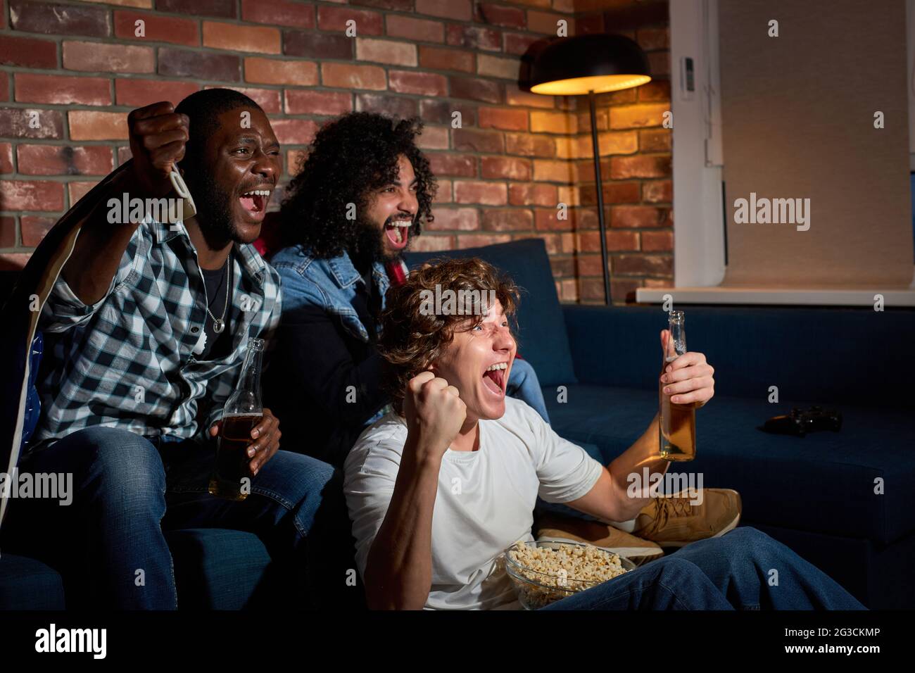 Junge Sportfans feiern den Sieg zu Hause. Leidenschaftliche Unterstützer brüllen beim Fernsehen, jubeln zusammen, brüllen emotional Stockfoto