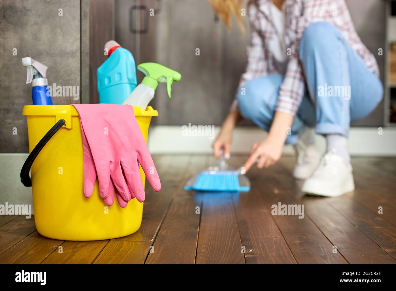 Konzentrieren Sie sich auf Eimer mit Gummihandschuhen und Waschmitteln im Inneren, weibliche Hausfrau entfernen Staub und Schmutz vom Boden mit Bürste und Kehrschaufel, Reinigung h Stockfoto