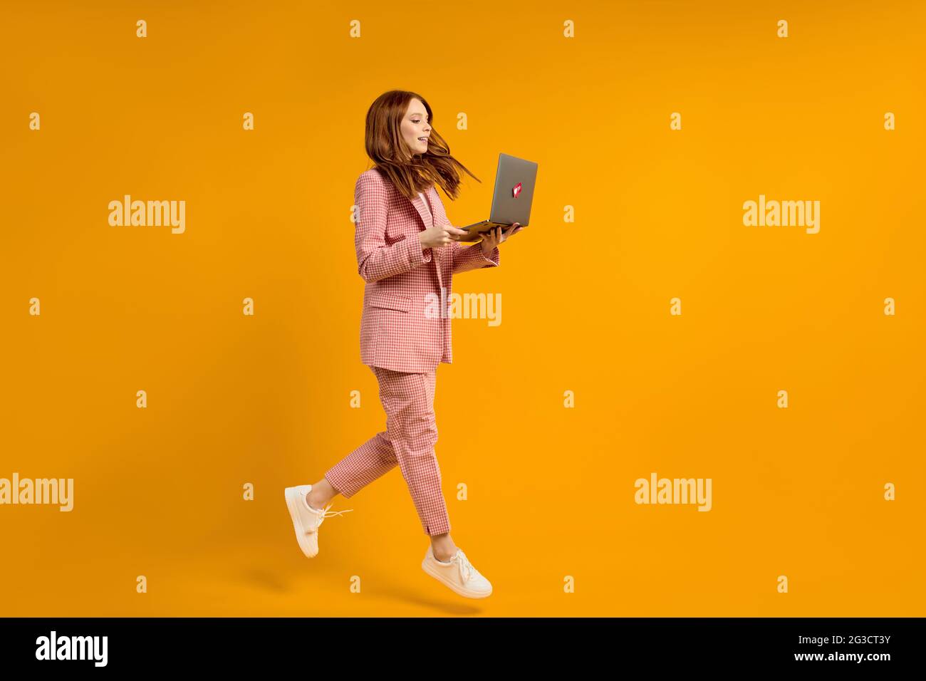 Aufgeregt springende Frau mit Laptop isoliert auf gelben Studio-Hintergrund. Moderne Technologien, Freiheit der Wahl Konzept, Emotionen Konzept. Mit Lapto Stockfoto