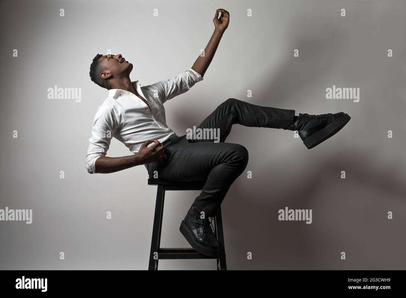 Ein fröhlicher junger schwarzer Mann, Model, sitzt auf einem hölzernen Spaß und gibt vor, Air-Gitarre zu spielen. Stockfoto