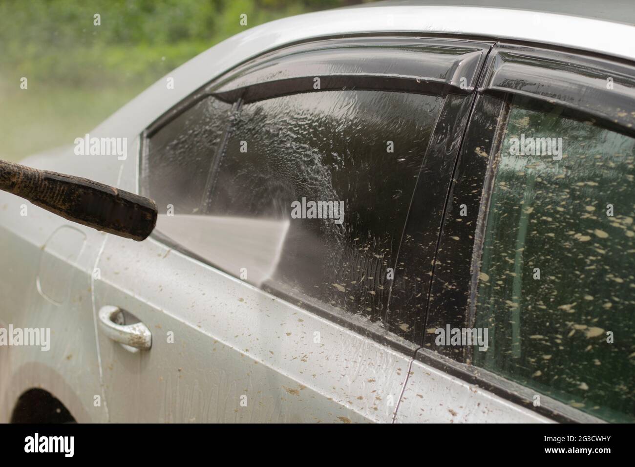 Autowäsche. Das Auto wird unter dem Druck eines Wasserstrahls gewaschen. Mit einem Wasserspray Schmutz von der Fahrzeugoberfläche abwaschen. Stockfoto