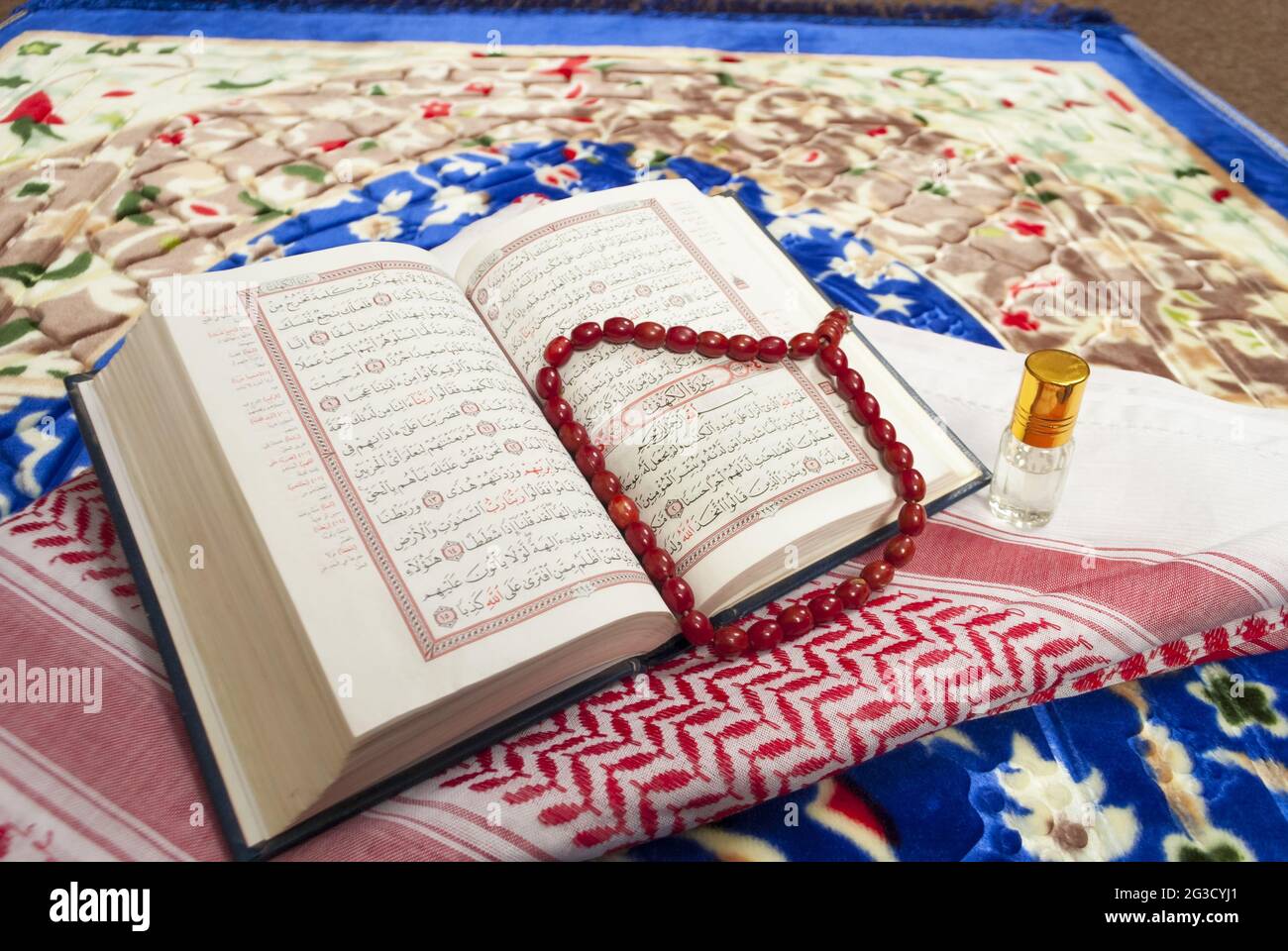 Nahaufnahme des islamischen Buches Koran Rosenkranz und shemagh Duftflasche auf bunten Gebetsmatte, religiöse Konzept traditionelle Accessoires Stockfoto