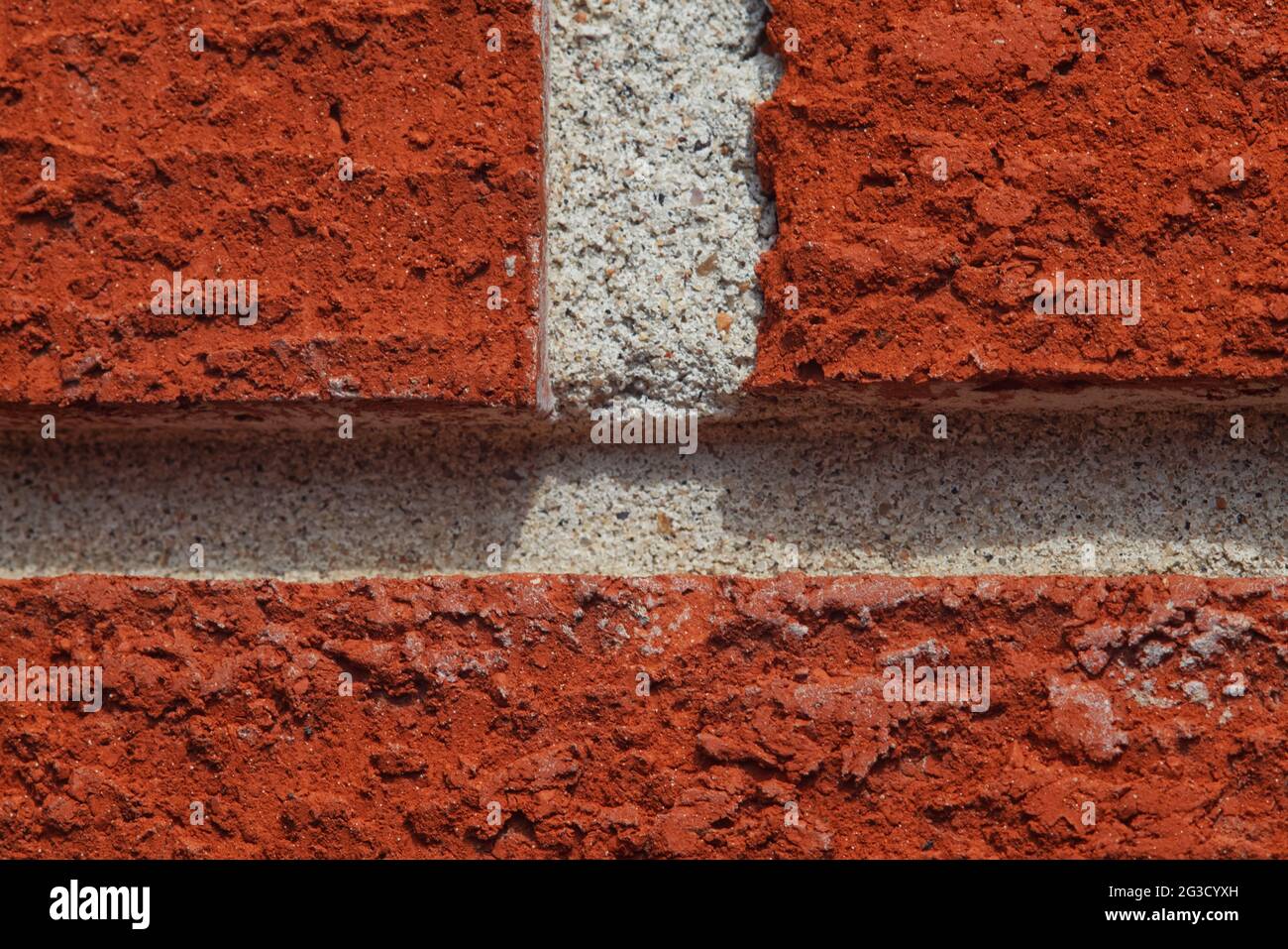 Eine Makroaufnahme aus leuchtend roten Ziegeln und weißem Mörtel in der Nachmittagssonne, die sich auf die holprige Textur der Steine konzentriert. Stockfoto