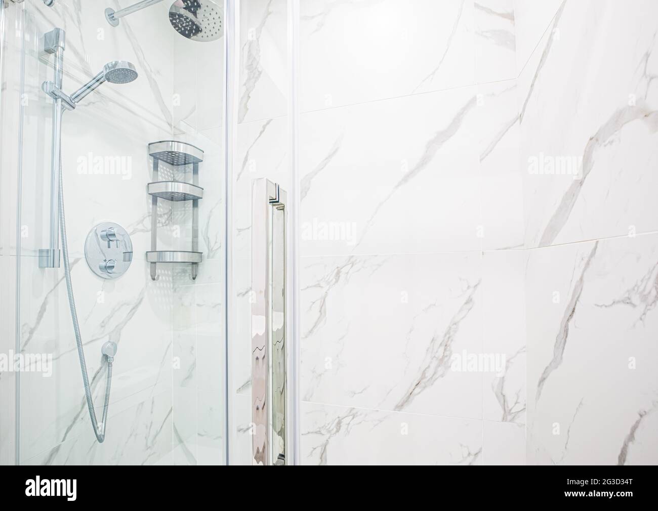Dusche in einem modernen Badezimmer mit Marmorwänden und klarem Glas auf der Vorderseite und abnehmbarem Duschkopf mit Metalldrähten und -Rohren Stockfoto