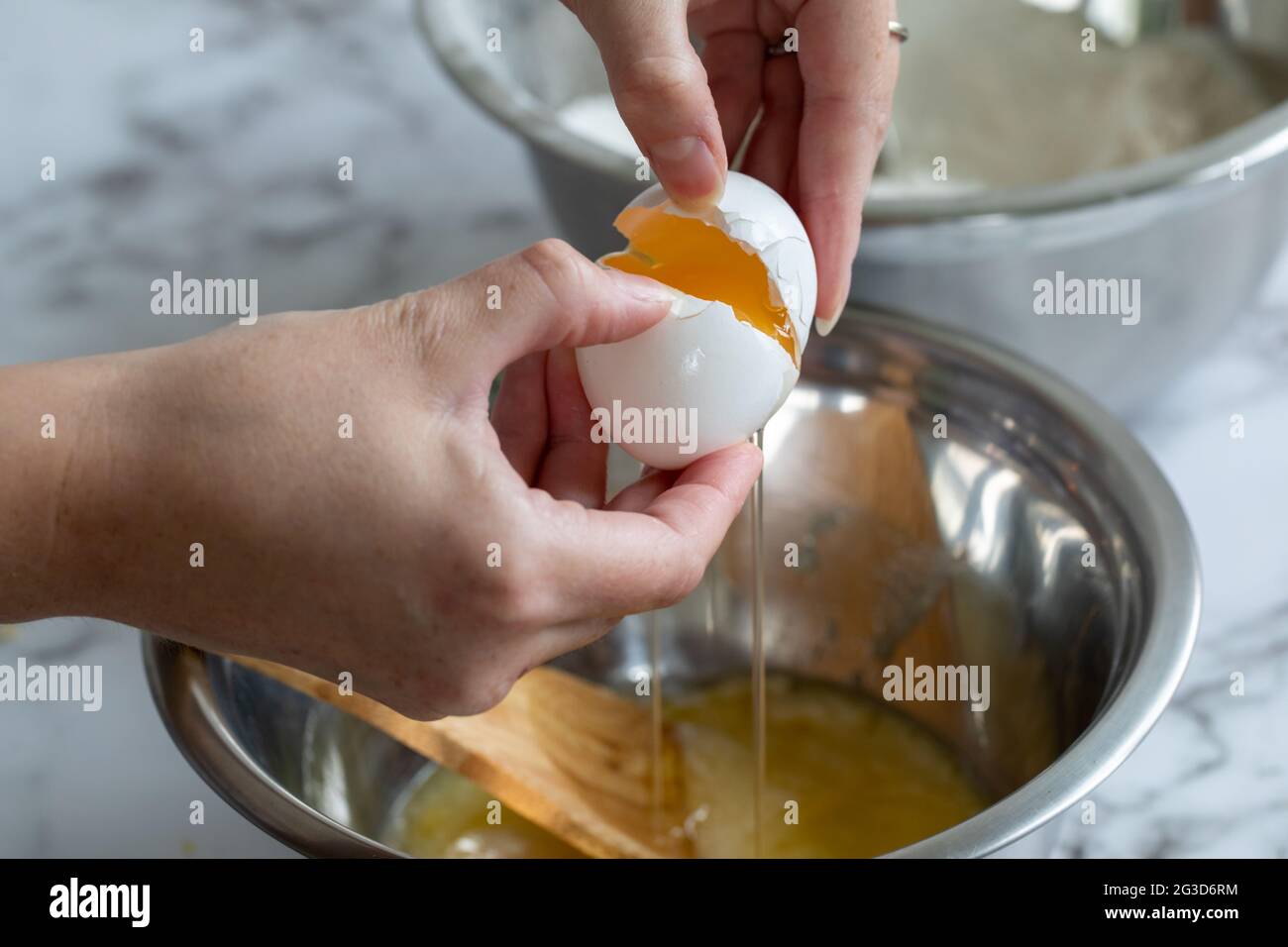 Die Hand einer Frau knackt ein Ei über einer runden Metallschüssel mit natürlichem Licht Stockfoto
