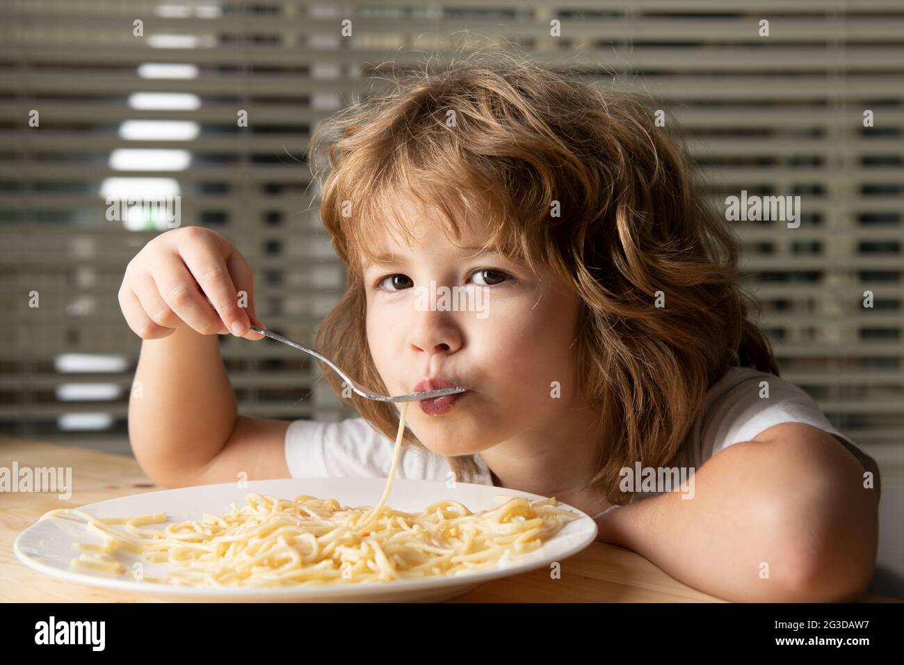 Kaukasisches Kind, das Nudeln, Spaghetti isst. Kinder lustiges Gesicht. Stockfoto