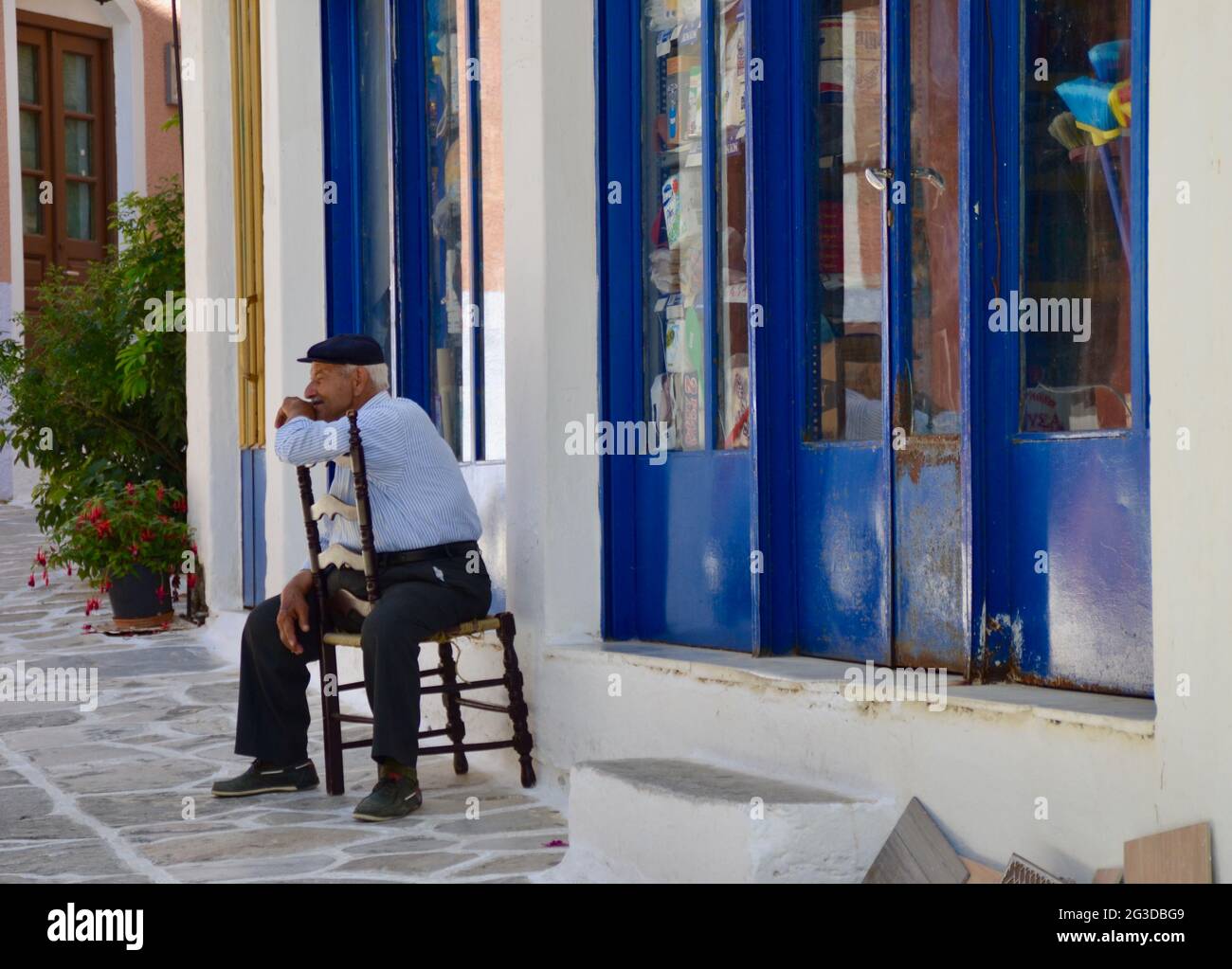 Ein alter griechischer Mann, der auf einem Stuhl in einer ruhigen Straße auf Naxos, Griechenland, sitzt Stockfoto