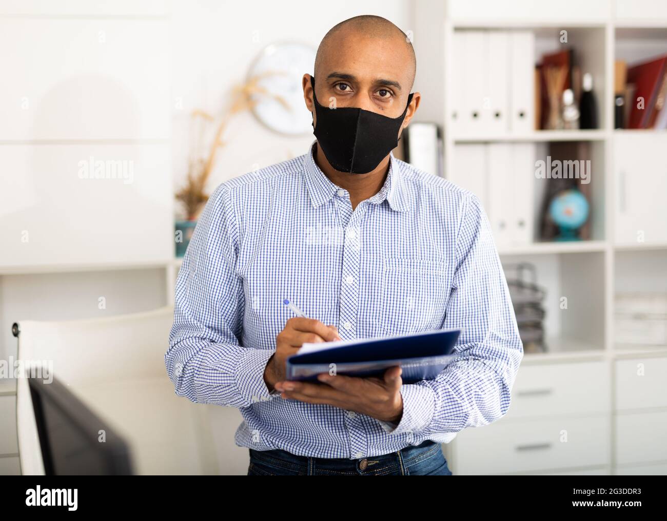 Geschäftsmann in Schutzmaske macht Notizen in Dokument Stockfoto