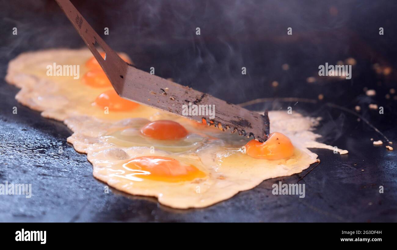 Nahaufnahme mehrerer Eier, die auf einem Grill oder Grillplatte gekocht werden. Eigelb wird von der bbq-Rutsche durchbohrt oder geklopft. Gebratene Eier werden gekocht. Stockfoto
