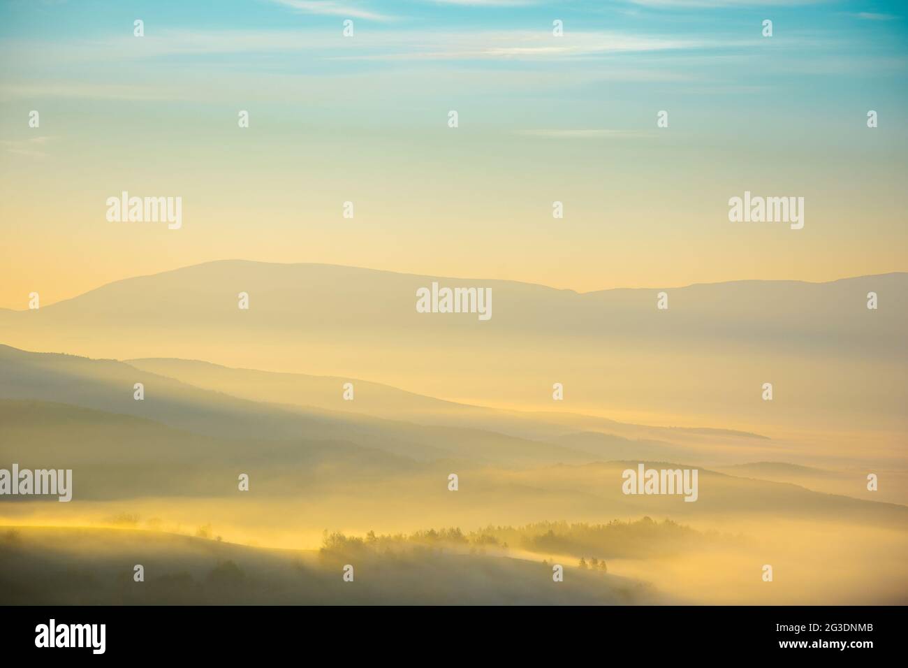 Bergige Landschaft bei nebligen Sonnenaufgang. Wunderbare herbstliche Naturlandschaft mit entfernten ländlichen Tal in glühenden Nebel. Bäume und Felder auf h Stockfoto