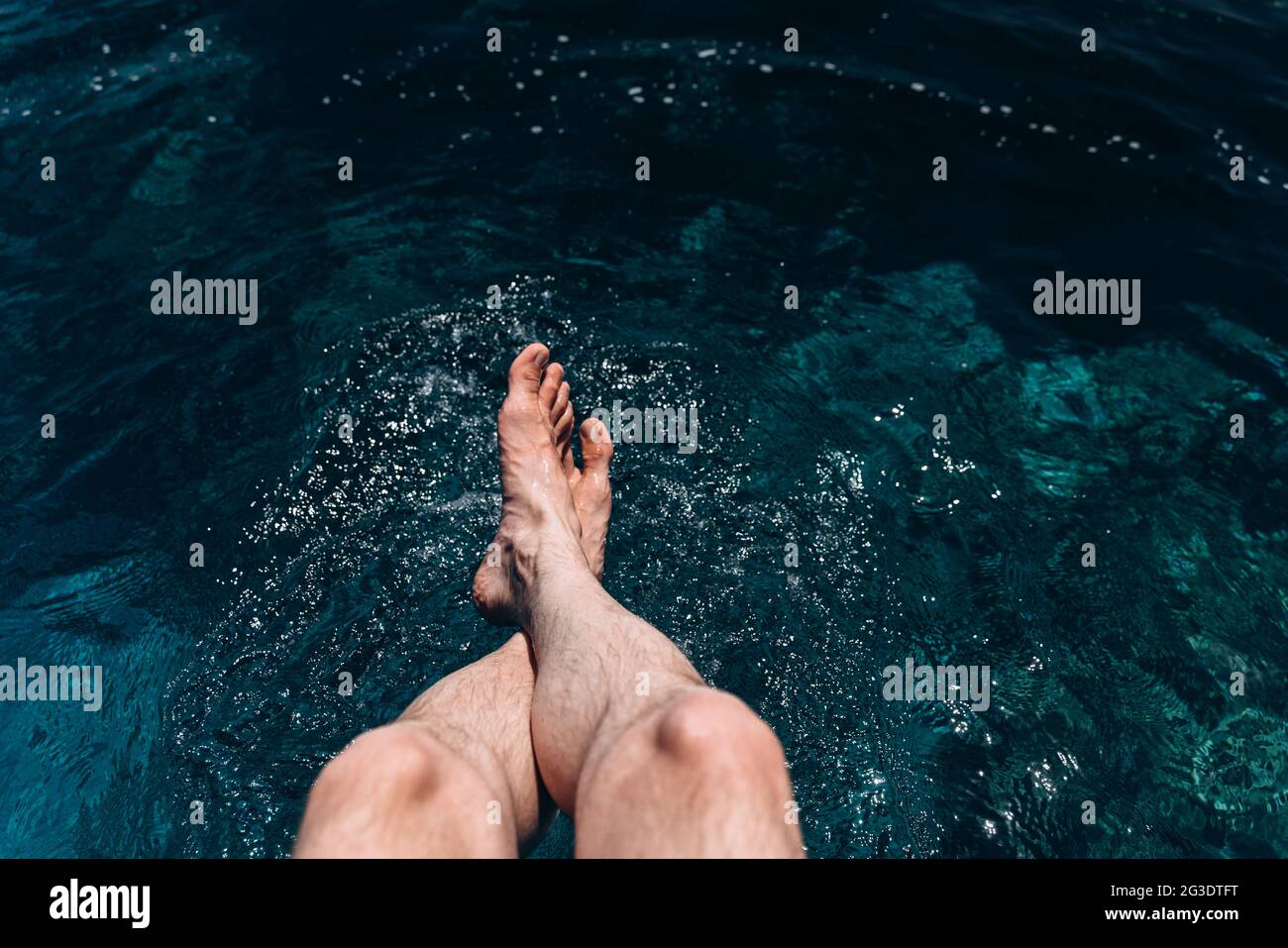 Gekreuzte, männliche Beine in das blaue Wasser abgesenkt. Entspannter Mann am Meer Stockfoto