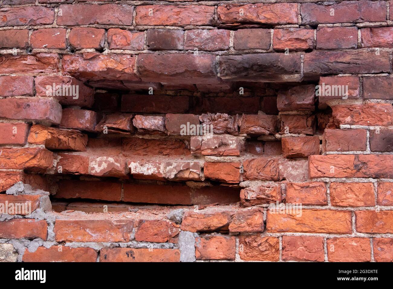 Alte halb zerstörte Steinmauer aus roten Ziegeln mit großem Schlagloch Stockfoto
