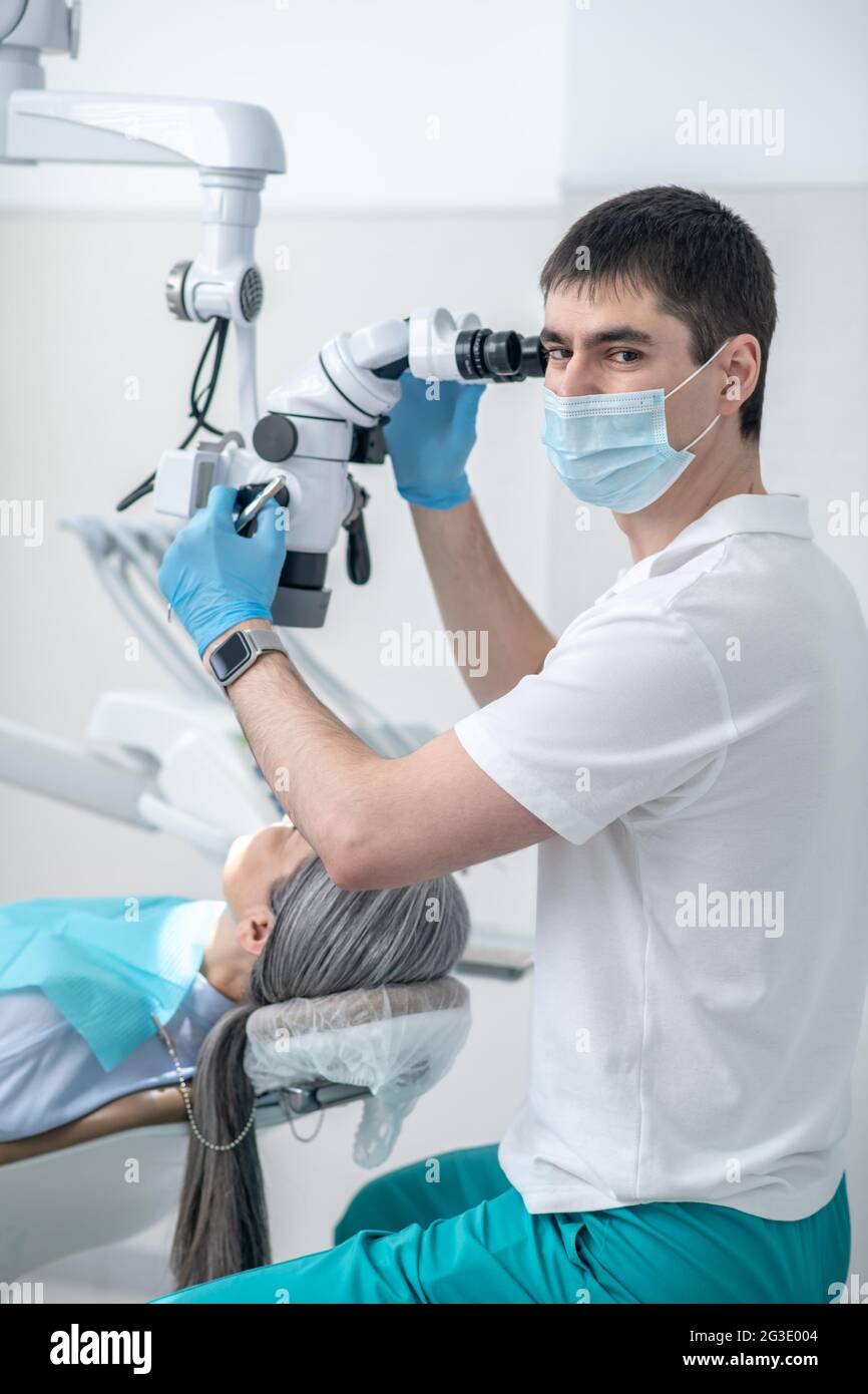 Männlicher Zahnarzt, der mit einem optischen medizinischen Instrument arbeitet, während er eine Zahnwiederherstellung macht Stockfoto