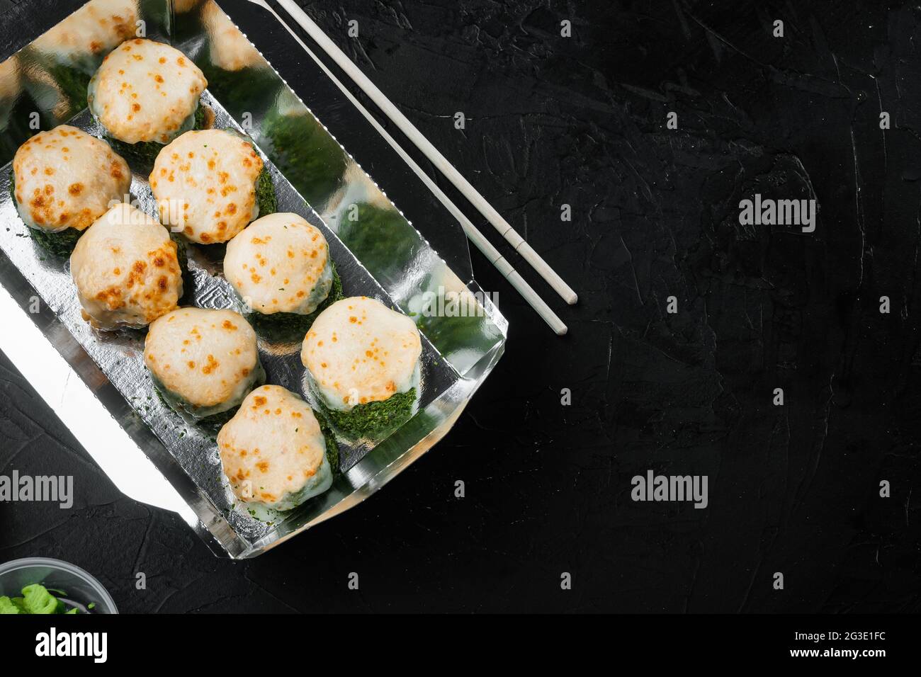 Sushi-Brötchen zum Mitnehmen in Behältern, philadelphia-Brötchen und gebackene Garnelenrollen auf schwarzem Stein-Hintergrund, mit Textrahplatz und Platz für Text Stockfoto