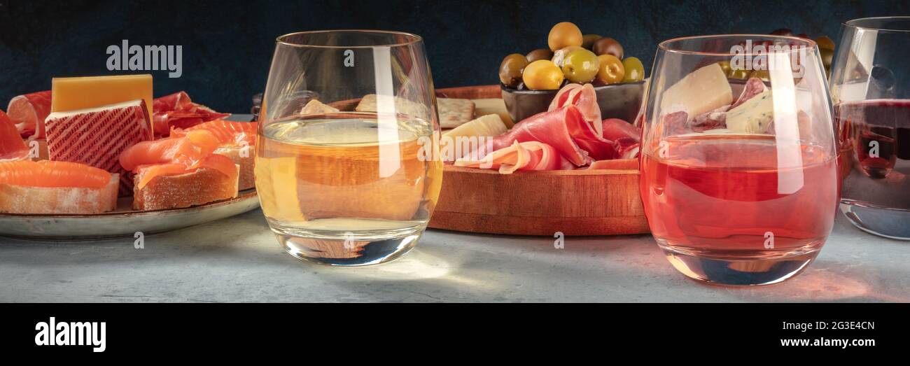 Italienische Antipasti oder spanische Tapas-Panorama mit Wein. Weiß- und Roséwein mit Prosciutto, Jamon, Käse, Lachs-Sandwiches und Oliven, ein Panorama-Header Stockfoto