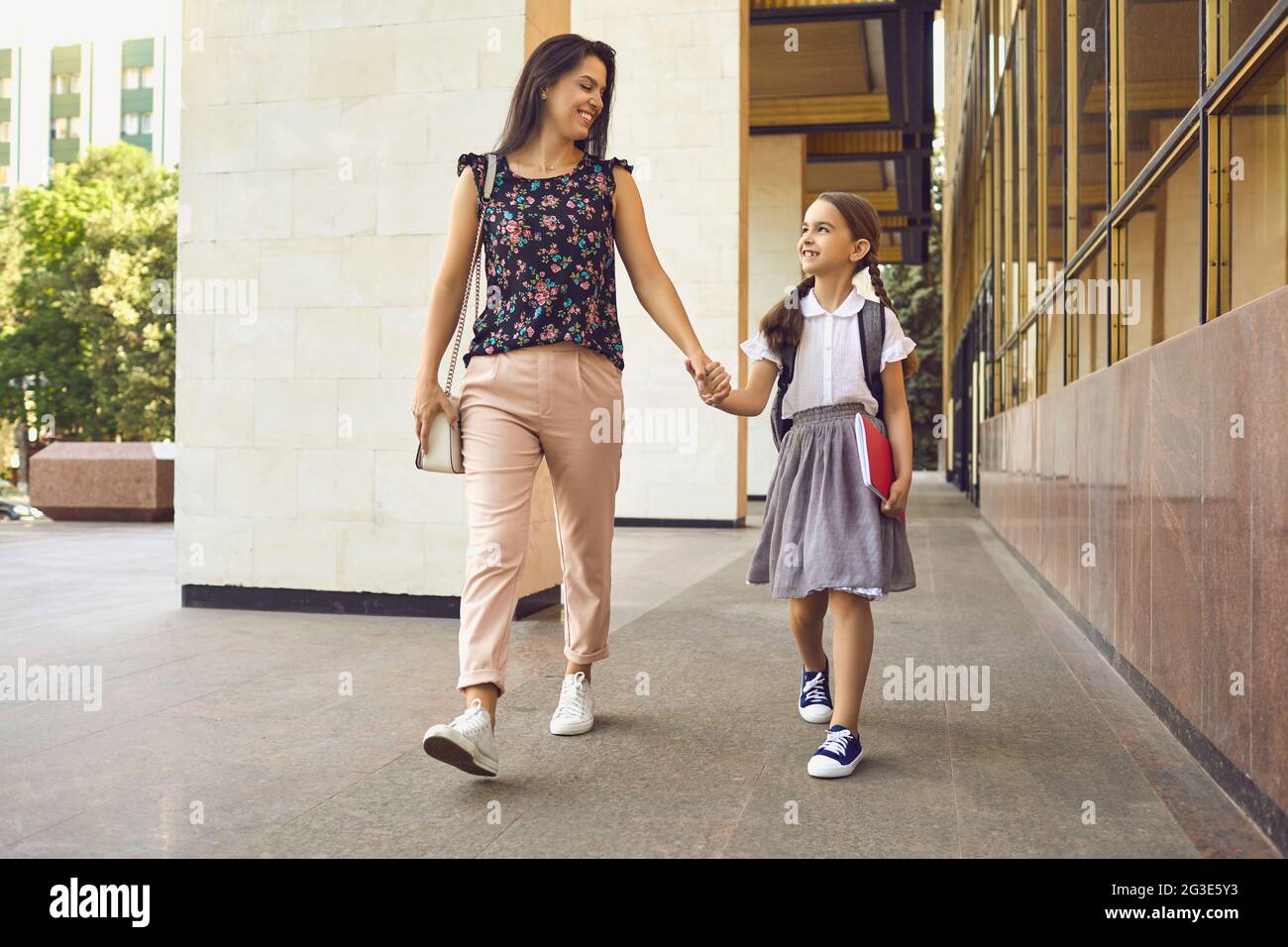 Lächelnde Mutter und Kind mit Rucksack gehen fröhlich zur Schule. Stockfoto