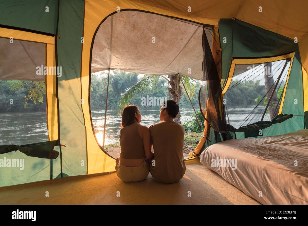 Junges asiatisches Paar, das sich abends in einem Zelt auf dem Campingplatz im Naturpark entspannt Stockfoto