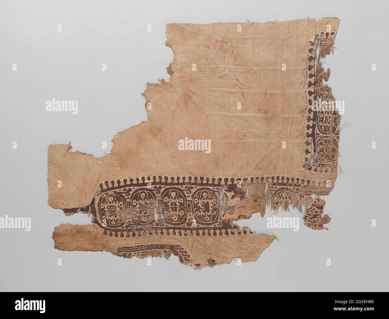 Gewebefragment mit Clavus. Natürlicher Leinenstoff mit Verzierung eines braunen Clavus. Der Clavus und die Tabula bestehen aus einem sich wiederholenden Kreismotiv mit einem unregelmäßigen Motiv mit sechs Cikels am Ende. Beim Clavus ist eine naturfarbene Lauffigur mit erhobener Hand gewebt. Die Kanten des Clavus bestehen aus einer durchgehenden Linie mit ausgezeichneten Stäben mit einer Stumpspitze. Im Leinengewebe werden aus etwa vier verdickten Einschlägen gewebt. 14 cm lang. Stockfoto