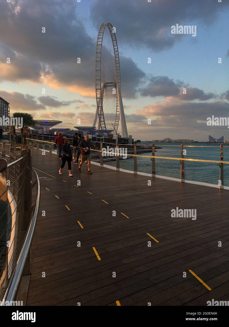 Wunderschöne Aussicht auf Touristen, die bei Sonnenuntergang auf der Brücke spazieren und Ain Dubai im Hintergrund. Stockfoto