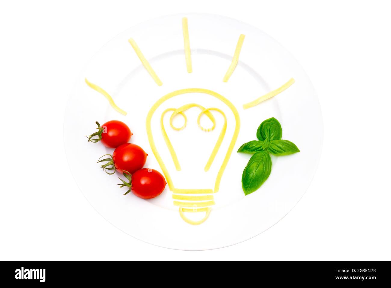 Kreative Lebensmittelkomposition: Weißer Teller mit einem leuchtenden Glühbirnensymbol aus gekochten Nudeln, Kirschtomaten und Basilikumblättern, isoliert auf Weiß. Stockfoto