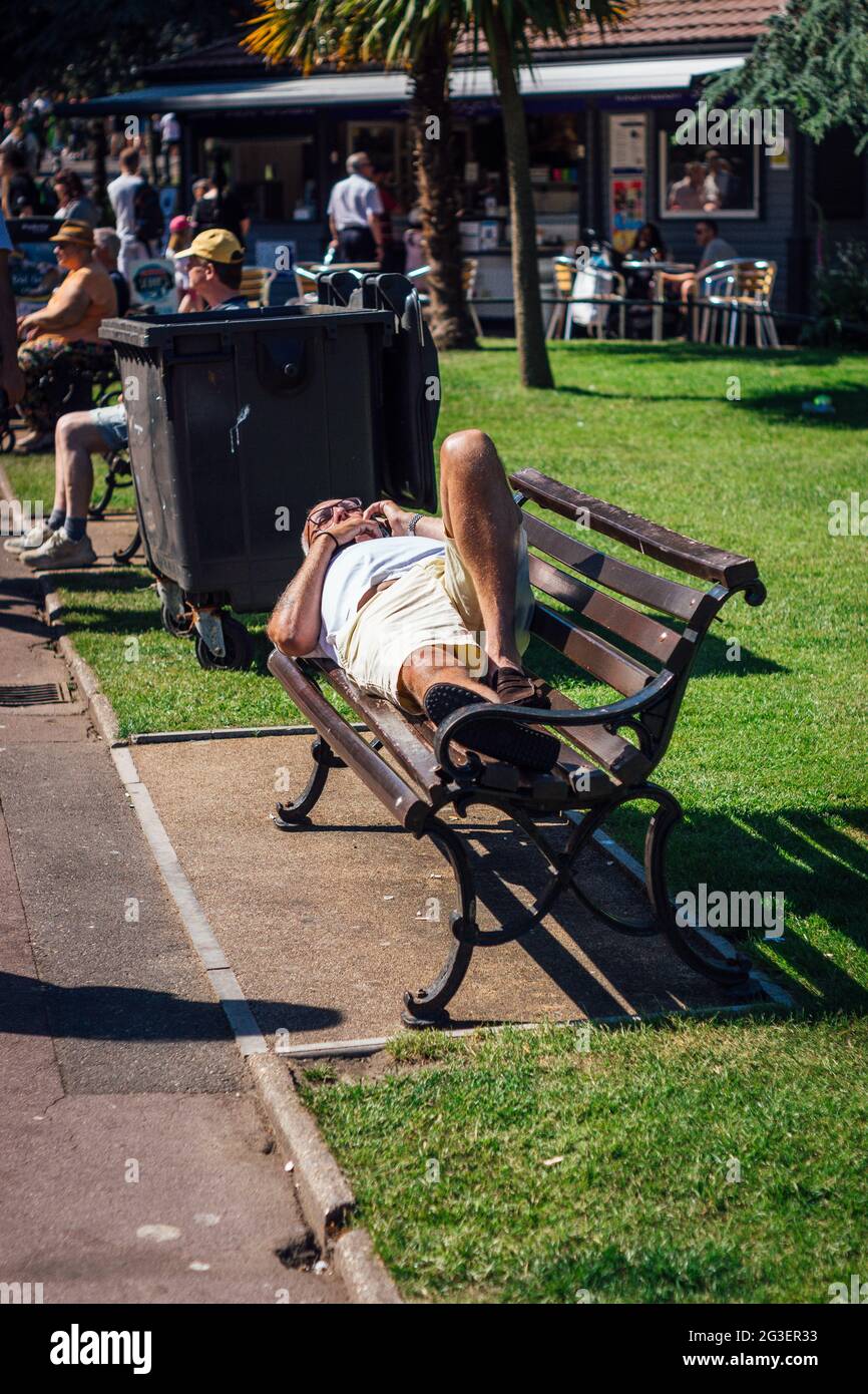 Älterer Mann, der auf einer Bank in Bournemouth Gardens, Bournemouth, Großbritannien, sonnenbaden geht. Stockfoto