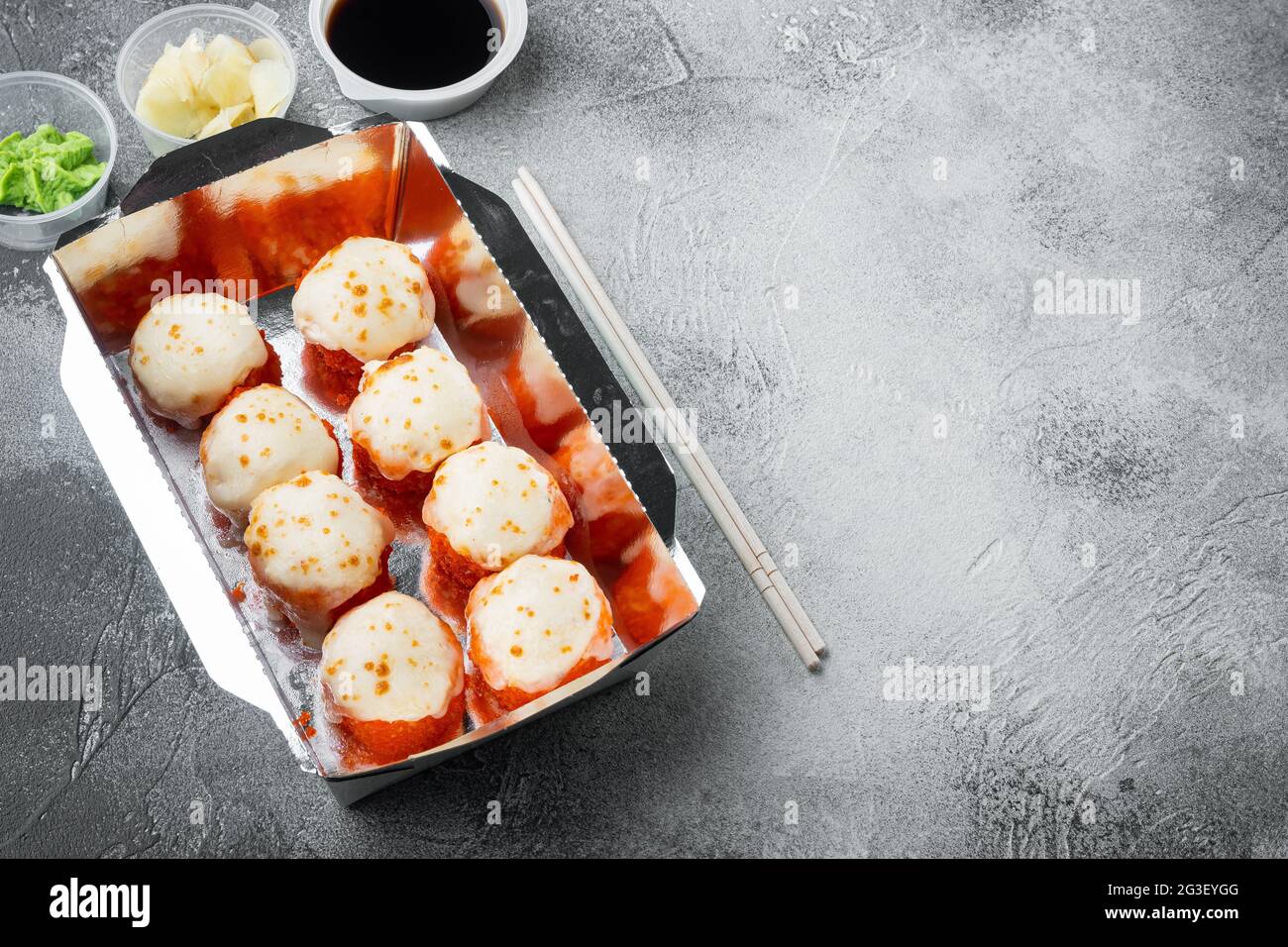 Leckere Sushi-Rollen im Einwegkarton-Set, auf grauem Steinhintergrund, mit Copyspace und Platz für Text Stockfoto