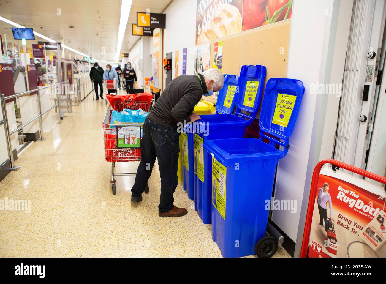 Der Freiwilligenarbeiter des Welcome Centers, Michael Blake, 70, sucht nach Lebensmittelspenden in den Sammelpunkten der Food Bank in Sainsbury’s Stockfoto