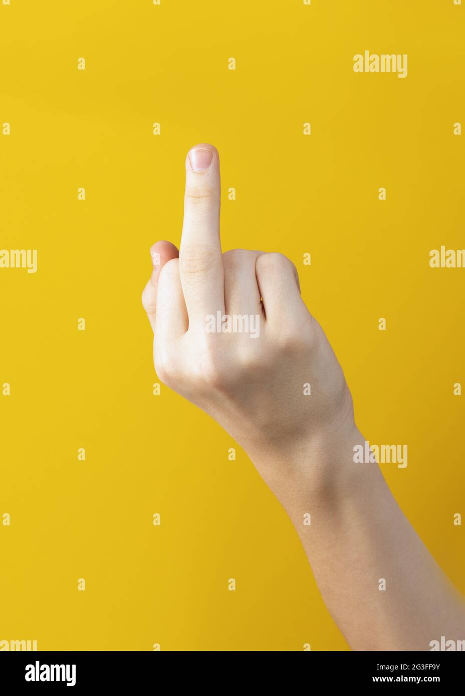 Weibliche Hand zeigt Mittelfinger auf gelbem Hintergrund. Geste drückt die Forderung aus, mich in Ruhe zu lassen Stockfoto