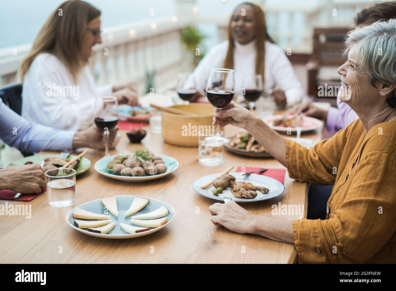 Fröhliche ältere Leute, die beim Barbecue-Abendessen im Freien mit Rotwein jubeln - konzentrieren Sie sich auf das richtige Frauengesicht Stockfoto