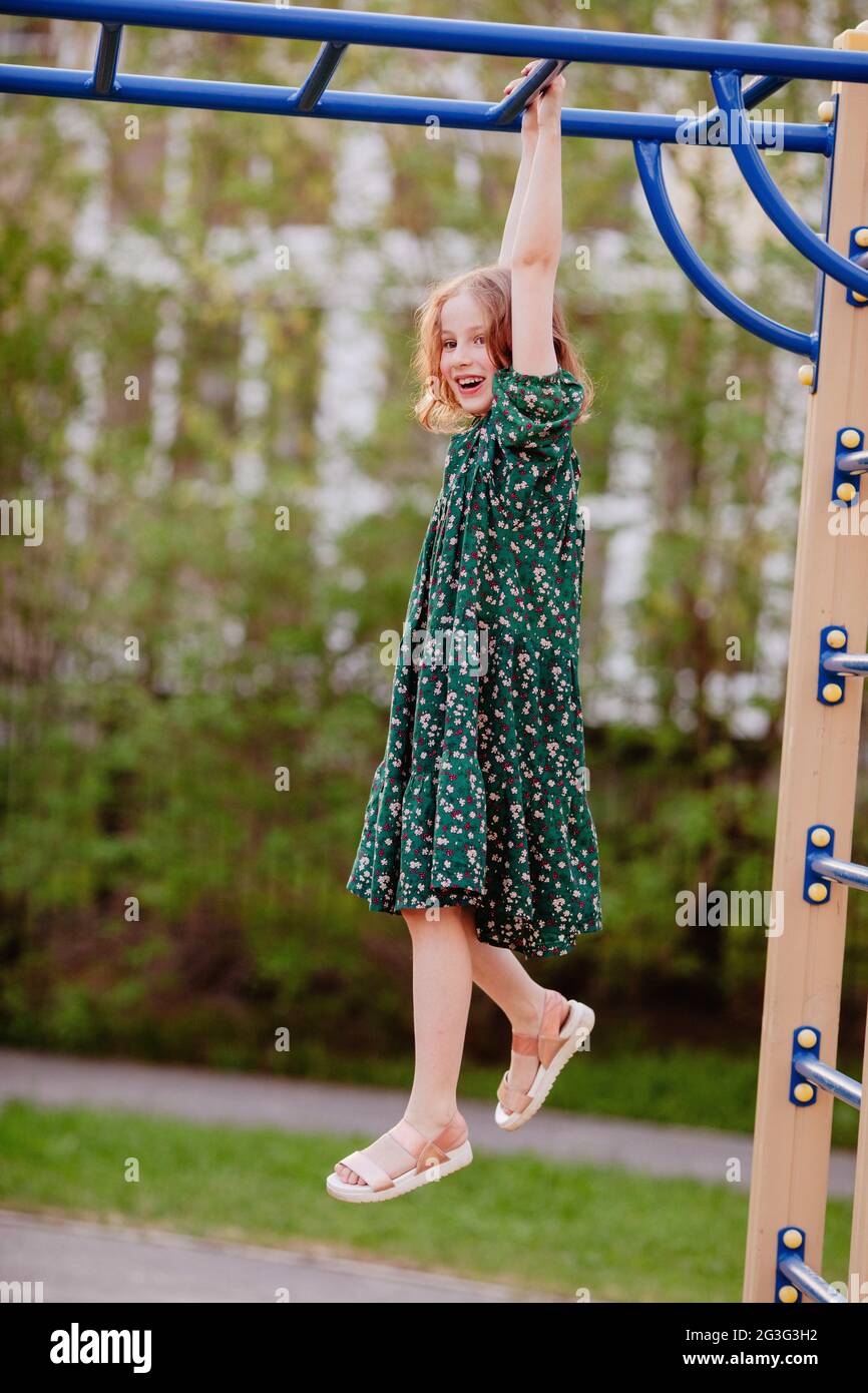 Seitenansicht der sorglosen Mädchen in Kleid hängen auf Metall-Affen Bars, während Spaß auf dem Spielplatz im Sommer Stockfoto