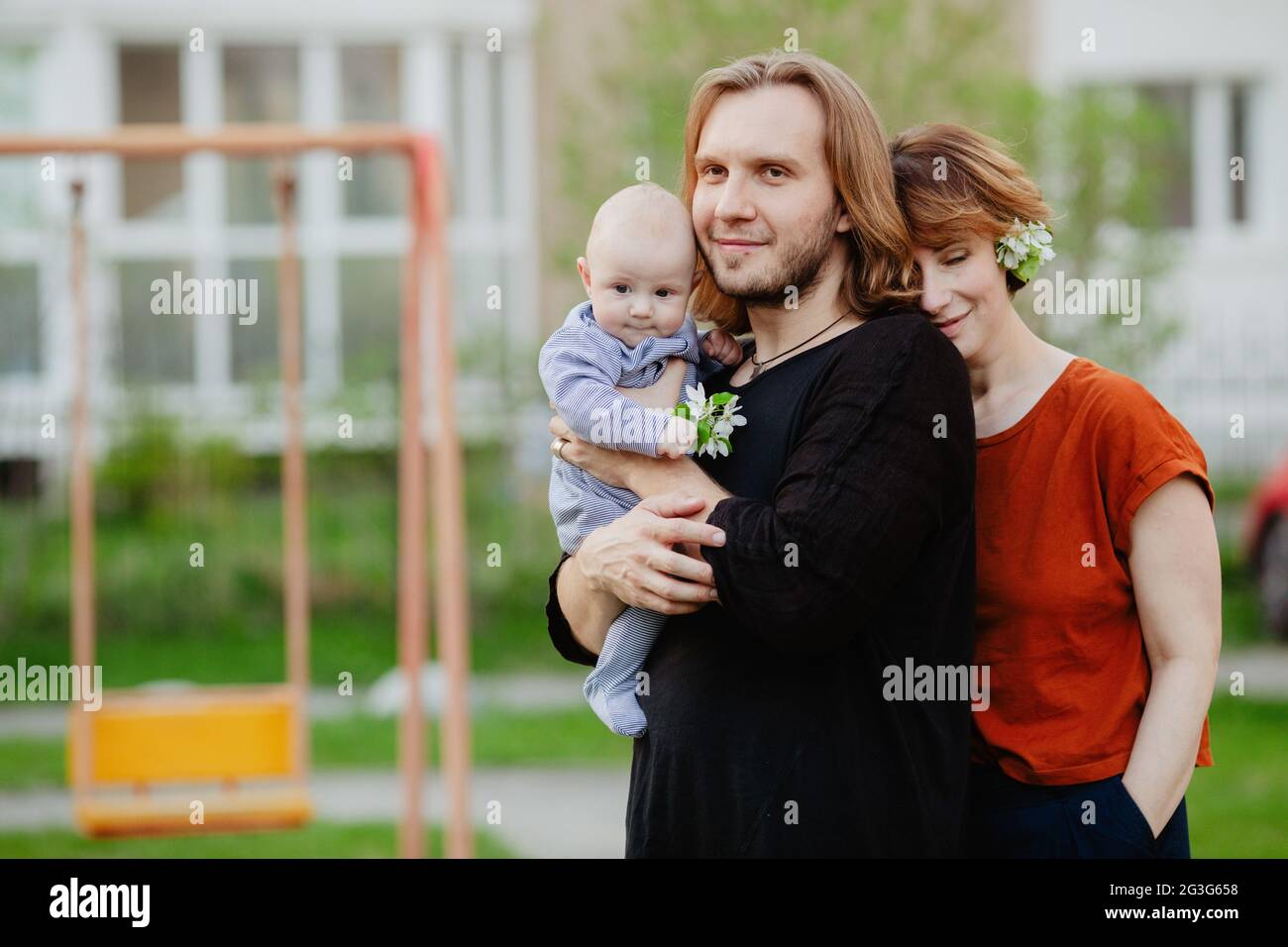 Lächelnde, zärtliche Mutter und Vater stehen mit einem entzückenden Kleinkind auf einem Spielplatz in der Stadt Stockfoto