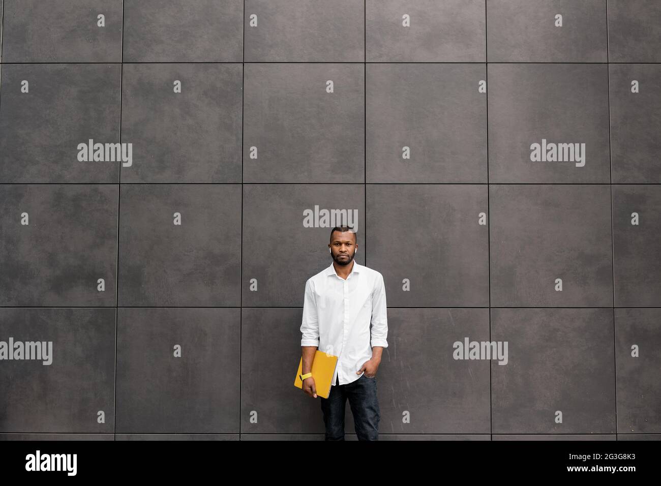 Fokussierter junger afroamerikanischer Geschäftsmann, Student oder Freiberufler, der mit einem gelben Laptop im Freien steht und sich für Online-Meetings aus der Ferne vorbereitet Stockfoto