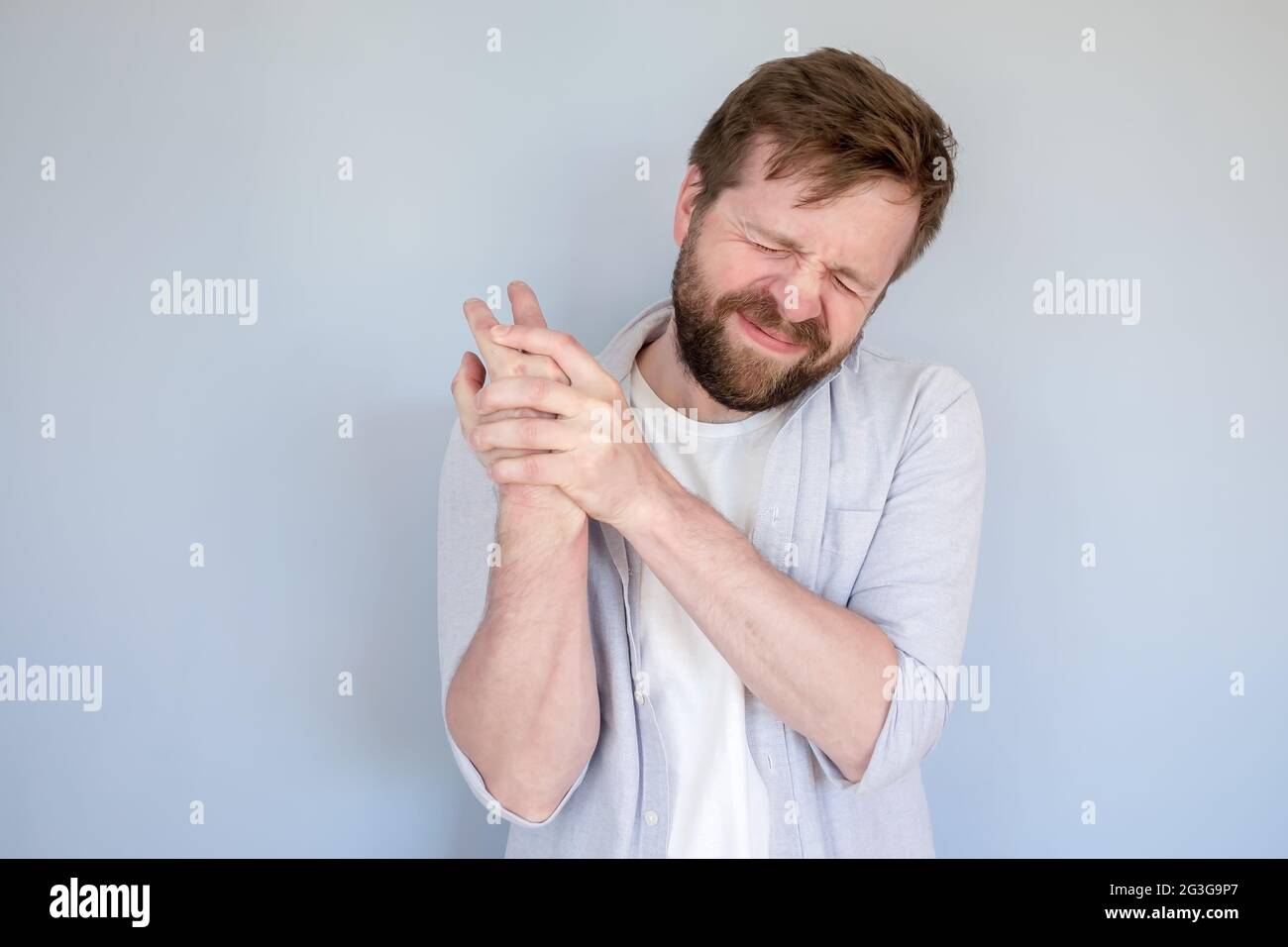 Bärtiger Mann hat starke Schmerzen im Arm, massiert die Wunde Stelle und schließt die Augen im Leiden. Medizinisches Konzept. Stockfoto