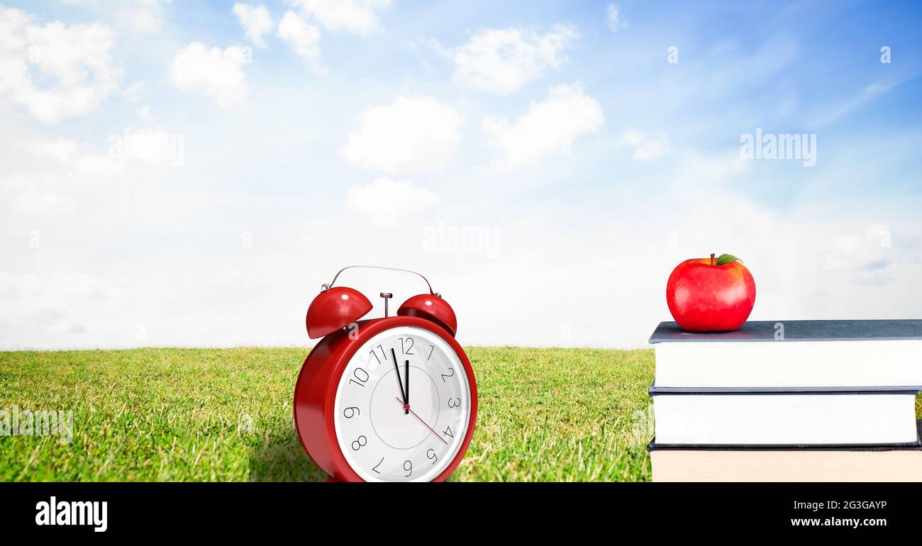 Apfel über Stapel von Büchern und roter Wecker gegen Landschaft mit grünem Gras und blauem Himmel Stockfoto