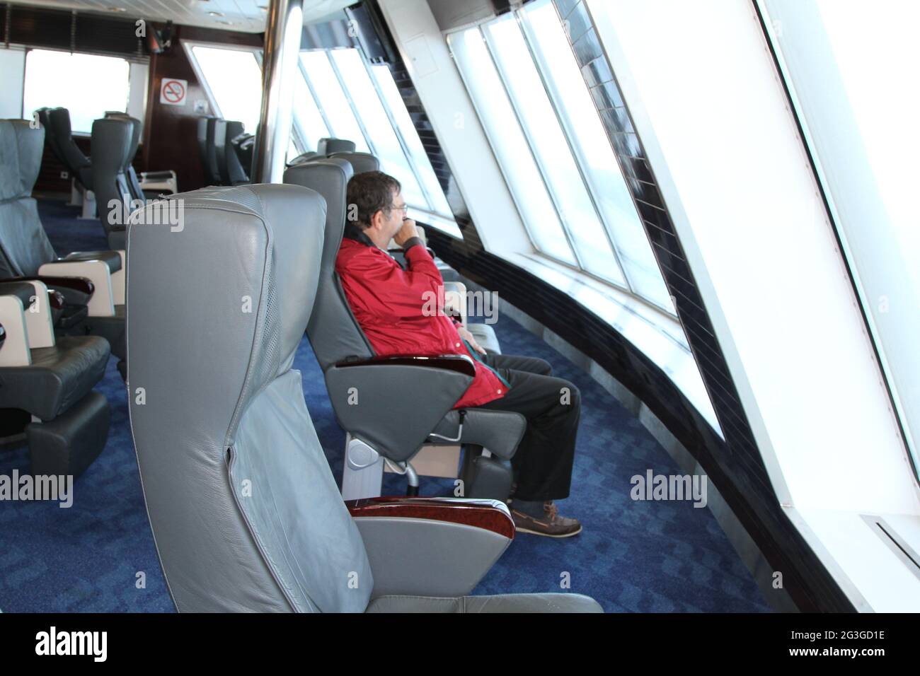 Mann, der auf einem Sitzplatz in einem Fährschiff sitzt und durch Panoramafenster blickt Stockfoto