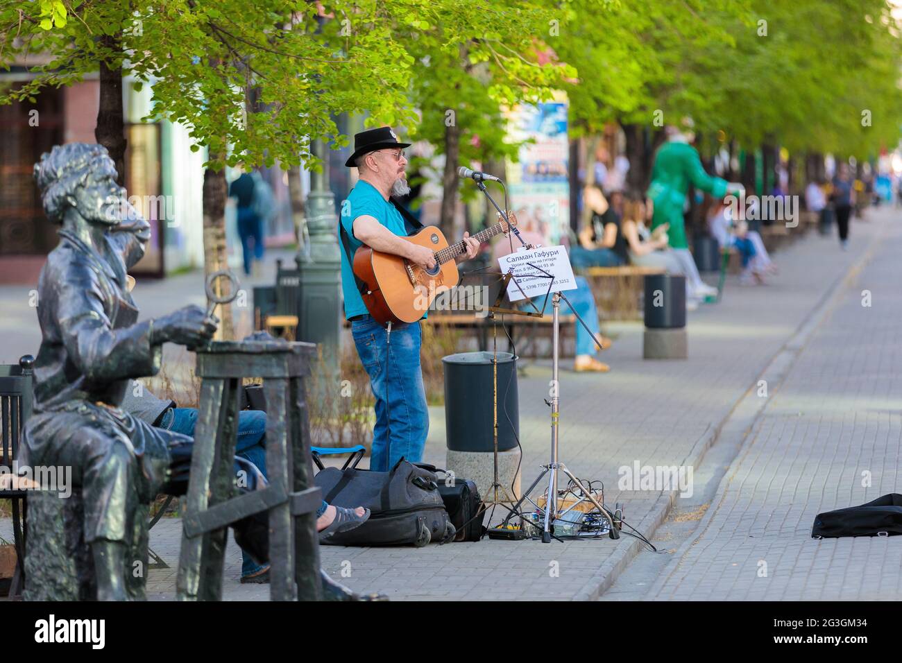 Ein erwachsener grauhaariger Mann spielt Gitarre und singt auf einer Stadtstraße. Straßenmusiker. Tscheljabinsk, Russland, 17. Mai 2021 Stockfoto