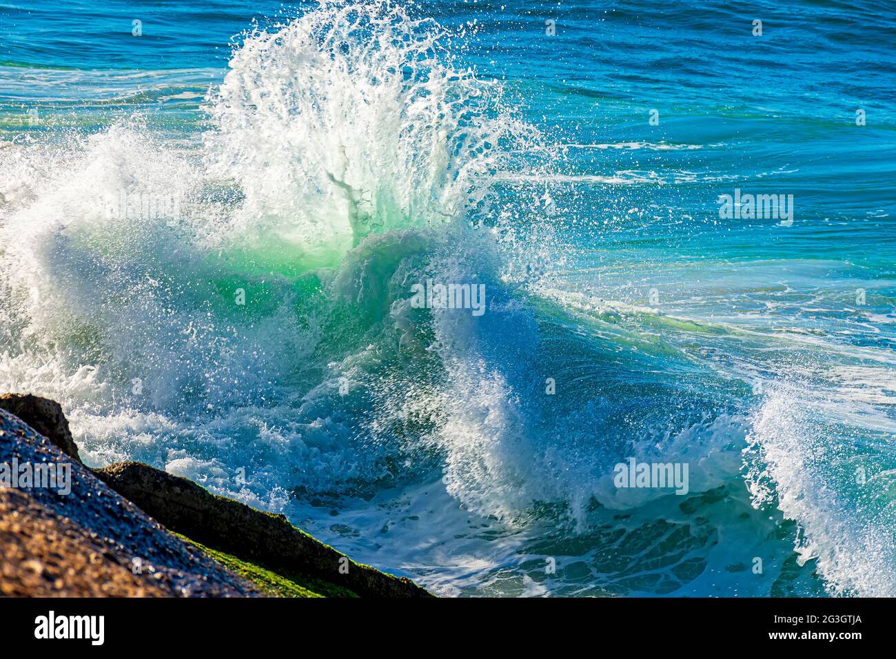 Wellen brechen in der Sommermorgendsonne gegen die Felsen am Strand Stockfoto
