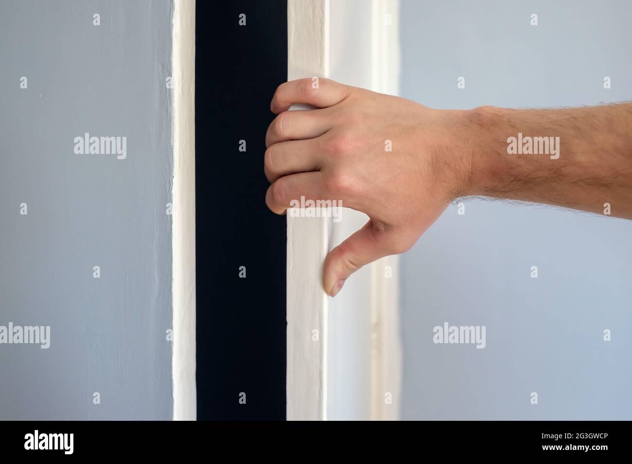Die Hand eines Mannes öffnet die weiße Tür eines blauen Schranks. Stockfoto