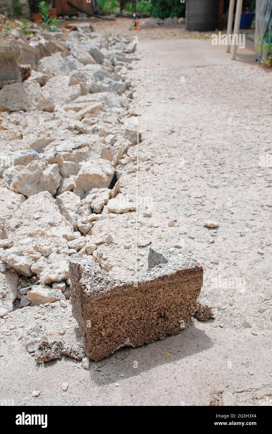 Ein Breeblock auf einer kleinen Baustelle im Inland. Der alte Beton wird aufgebrochen, bereit, das neue Fundament zu legen, der Breezeblock hält ein Maßband Stockfoto