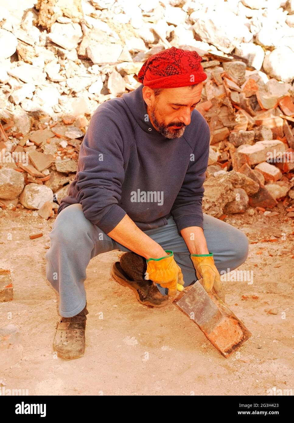 Ein Mann kratzt überschüssigen Zement von antiken Ziegeln ab, die für weitere architektonische Zwecke von der Abrissstelle eines alten italienischen Bauerngebäudes gerettet werden. Stockfoto