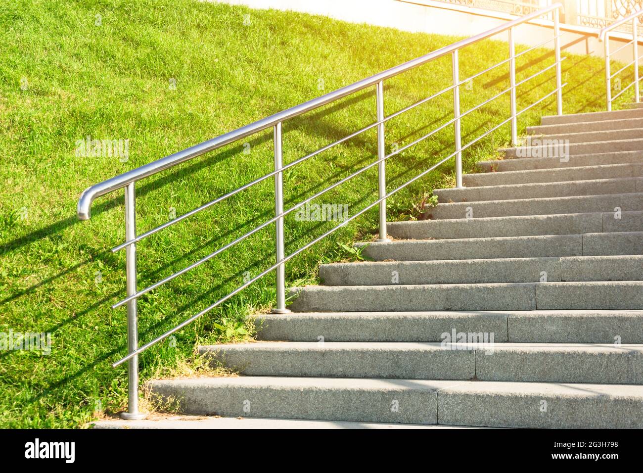 Steintreppe, die den Hang mit Rasengras, glänzendem Metall und Geländer  hinauf führt Stockfotografie - Alamy