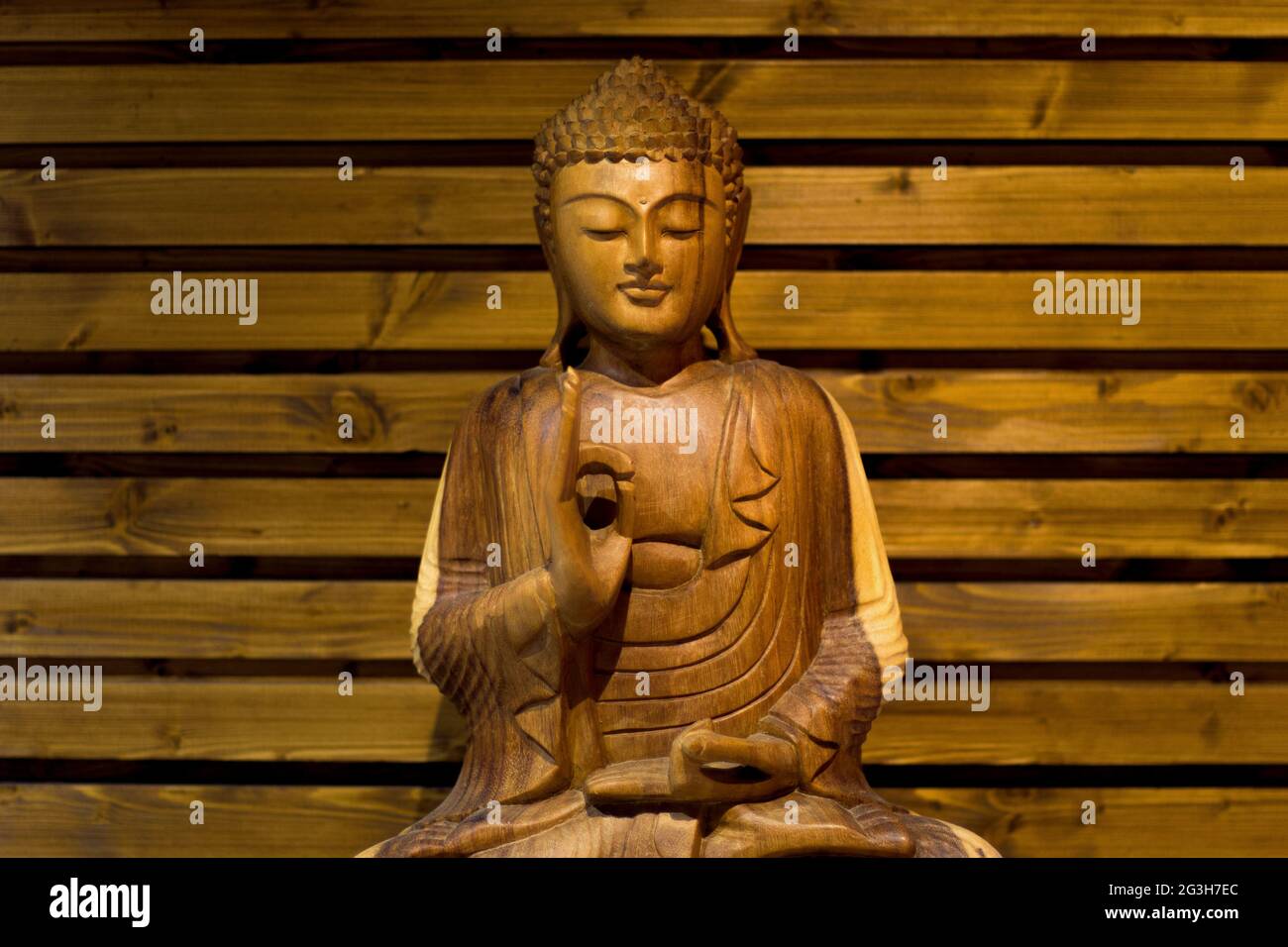 Beleuchteter Buddha aus Holz, der auf einem hölzernen Hintergrund meditiert Stockfoto