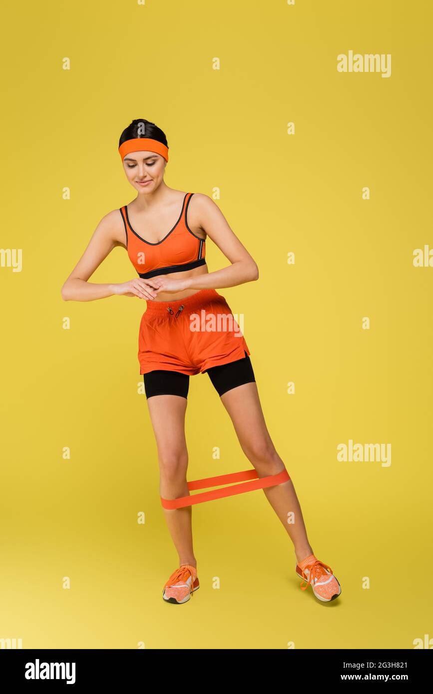 Junge sportliche Frau arbeitet mit Gummis auf gelbem Hintergrund Stockfoto